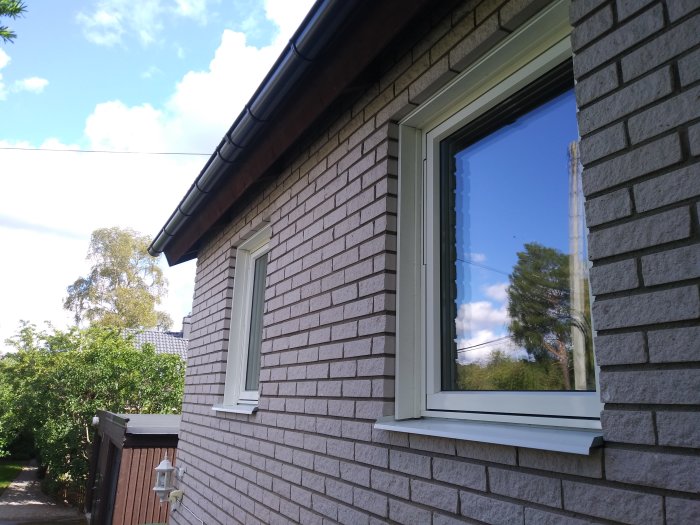 Husvägg med tegelimitation och träfönster med vitmålade foder i solljus.