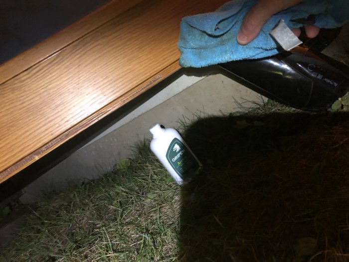 Hand som gnuggar limrester på dörr med trasa, acetonflaska och hårfön i förgrunden.