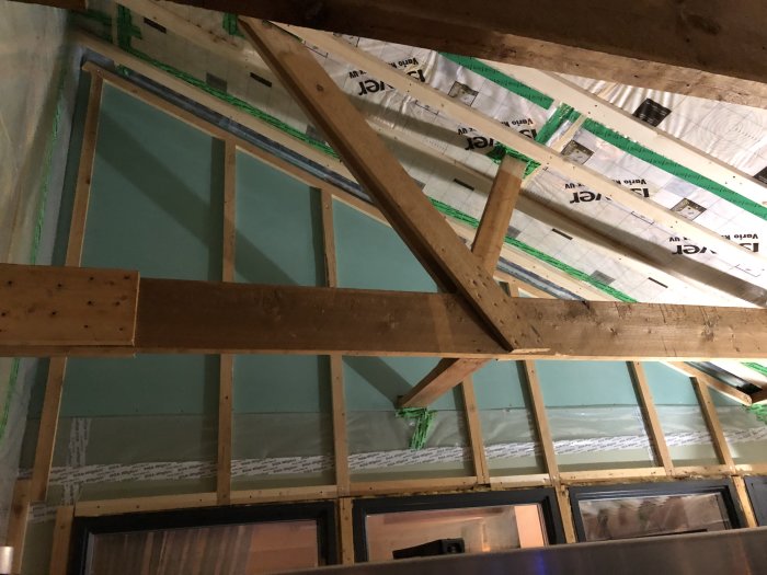 Tak och vägg under konstruktion med isolering och träreglar synliga, redo för slipning och elinstallation.