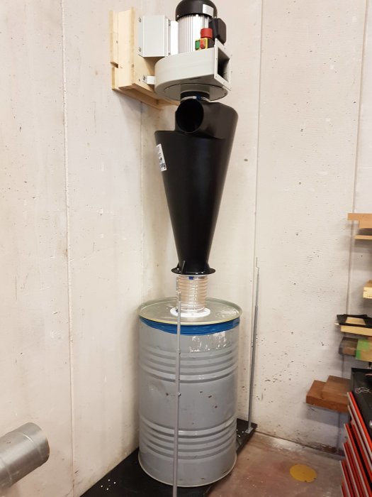 Cyclone dust separator mounted on wall above a collection barrel in a workshop.