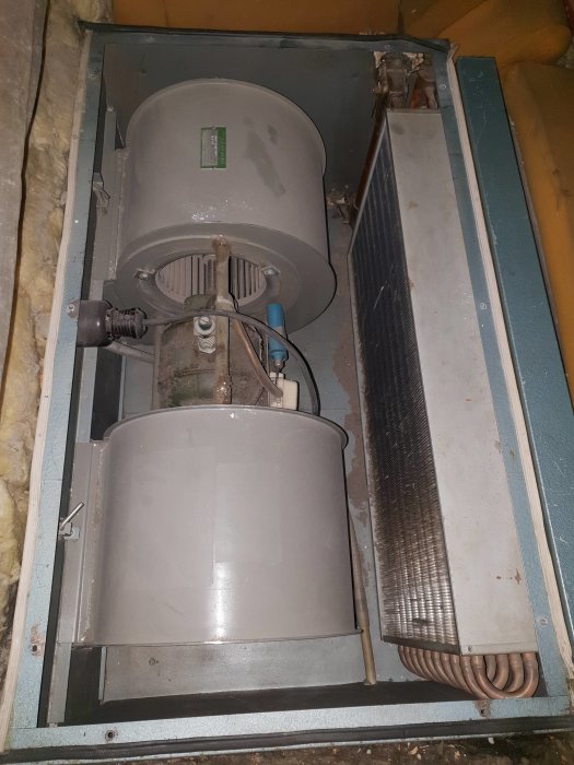 Gammal värmefläkt på vind med synliga rör och isolering, märkt som orsaken till hög energiförbrukning.