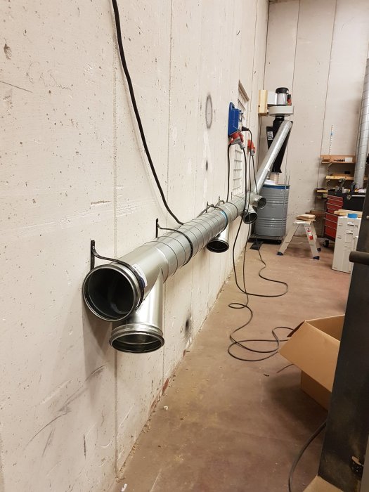 Installation av ventilation med flera metallsjokt rör som går längs en vägg i en verkstad eller ett garage.