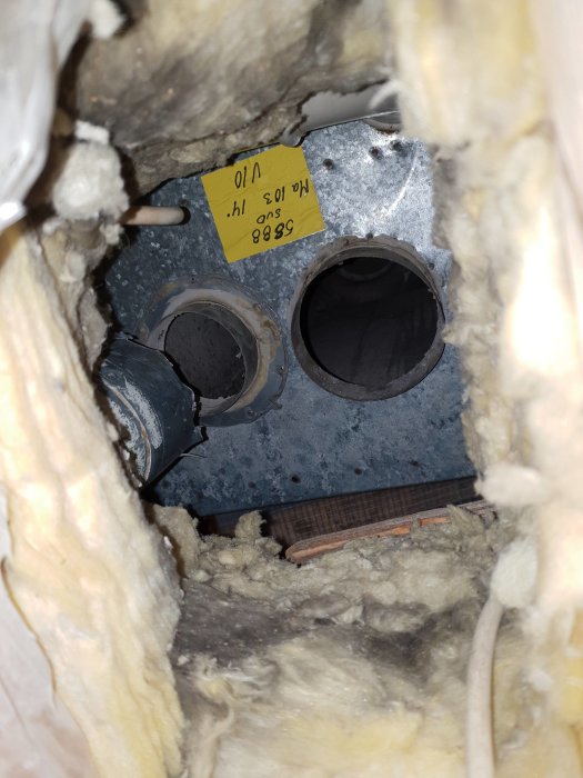 Vy av öppna ventilationskanaler och isolering på en vind med en etikett som syns.