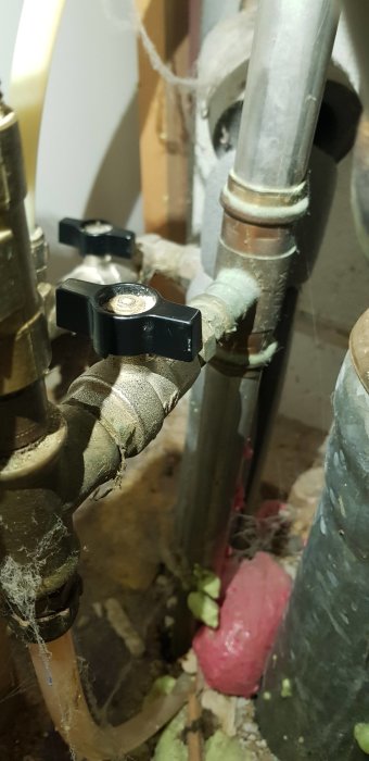 Stängda vattenkranar under handfat, omgivna av isolering och rör.