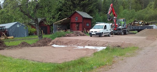 Grävarbetsplats med grushögar, vit skåpbil och liten grävmaskin vid markförberedelser.