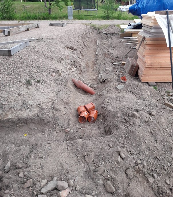 Grävd träningsgrop med orangea avloppsrör och omgivande byggmaterial på byggarbetsplats.