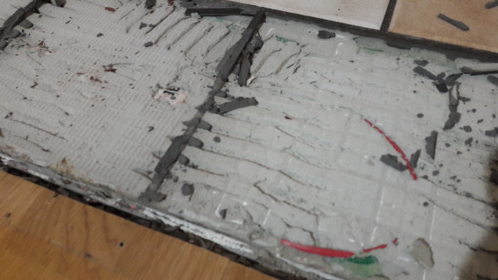 Golv med borttagen klinker och framträdande värmekabel i fix, redo för renovering.