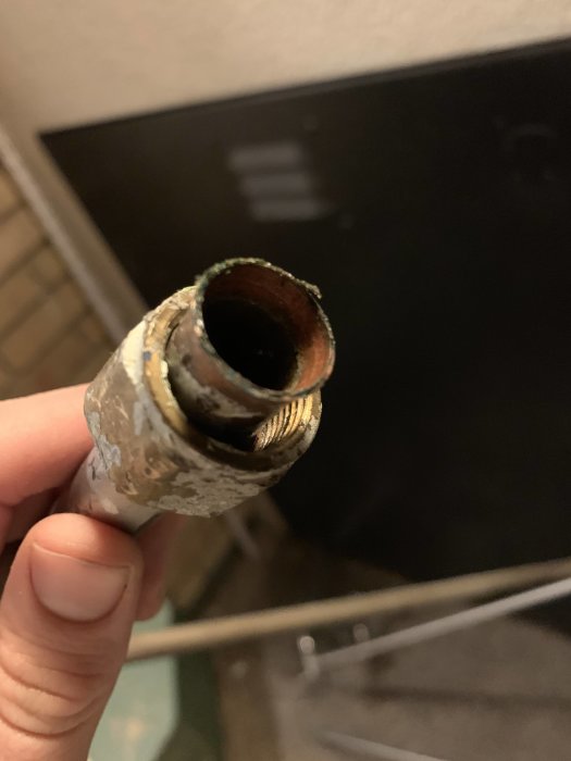 Hand håller ett gammalt rostigt rör med gängor som varit anslutet till ett t-rör.