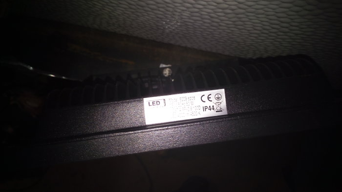 LED-armatur med etikett som visar 2x50W IP44, delvis i skugga mot en texturerad bakgrund.