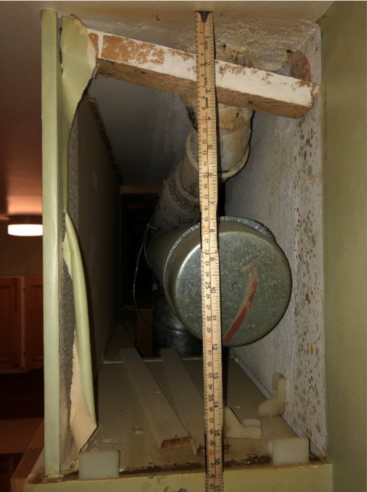 Mätsticka visar höjden på en öppnad vägg med synligt avloppsrör och ventilationskanal i ett renoveringsprojekt.