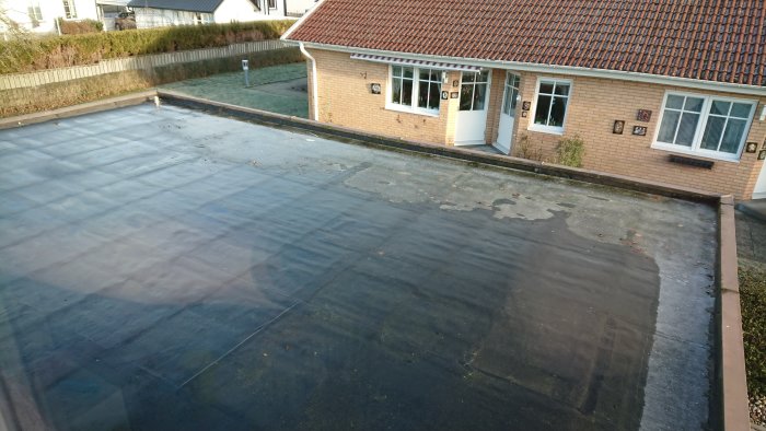 Gamla takpappen på ett garagetak med vattenpölar som inte dränerar ordentligt.