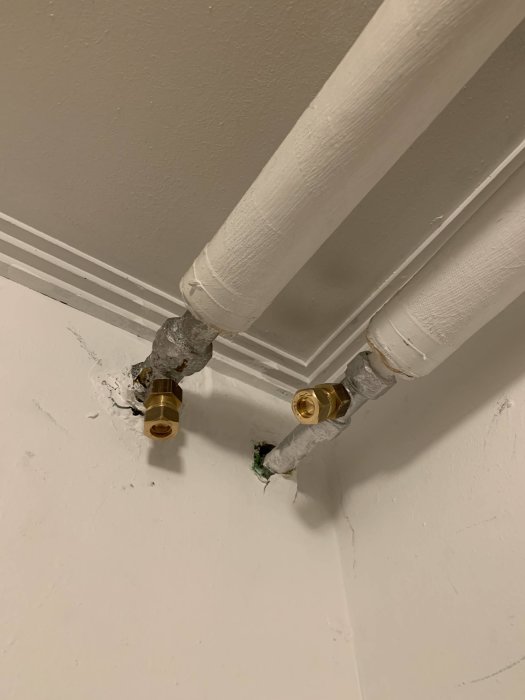 Två nyinstallerade röranslutningar med guldiga konor mot en vit vägg.