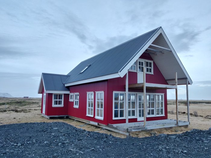 1,5-plansvilla med röd fasad och grått tak på Island, exteriör vy som visar fönster och farstukvist.