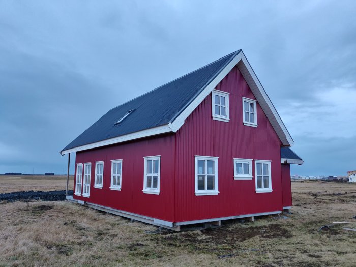 Rödmålad 1,5-plansvilla med svart tak, vitfönstrade på Island i dagsljus, omgiven av gräs.