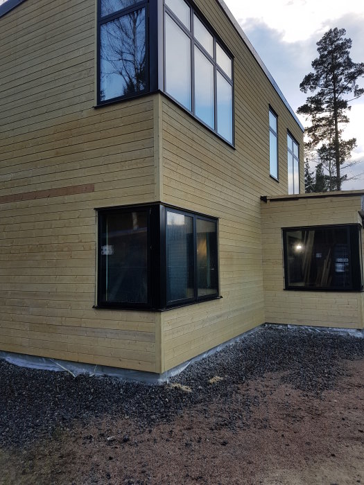 Ett hörn av ett nybyggt hus med träpanelväggar och stora fönster, ställning avlägsnad, vinter.