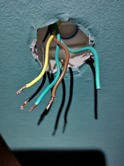 Elektriska kablar med olika färger som sticker ut från en vägg utan strömbrytare.