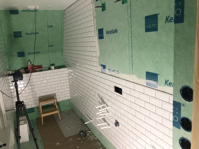 Badrum under renovering med halvsatt vitt kakel och synliga gröna väggskivor.