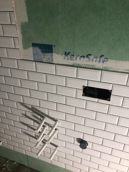 Vägg med nyinstallerad vit kakel och distanser använda för testläggning av plattor.