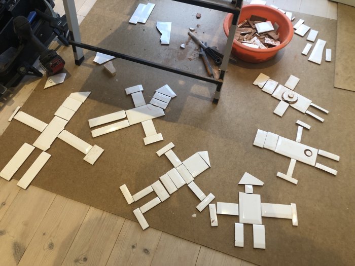 Kakelplattor ligger på golvet i form av figurer, verktyg och skärvor syns, testläggning av kakel.