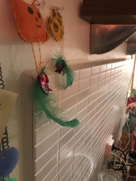 Dekorativa handgjorda figurer hängande på en vit kakelvägg i ett kök.