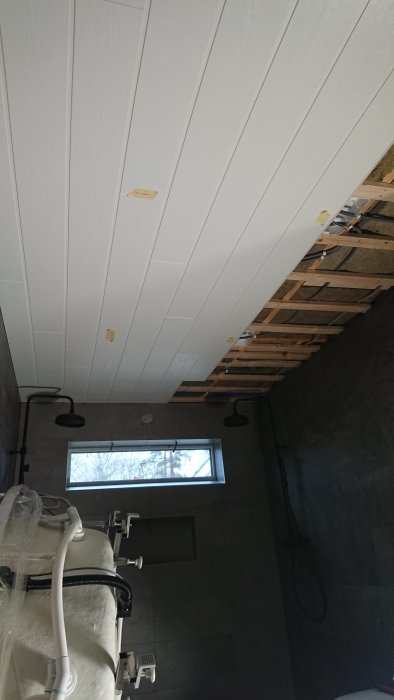 Nyinstallerat vitt tak i badrum med synlig träregelstomme och svarta badrumsarmaturer, inbyggd belysning och ett fönster.