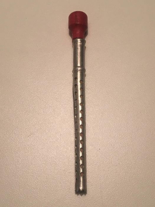 Aluminiumsverktyg med taggig ände och röd topp, möjligen för matlagning eller kryddning.