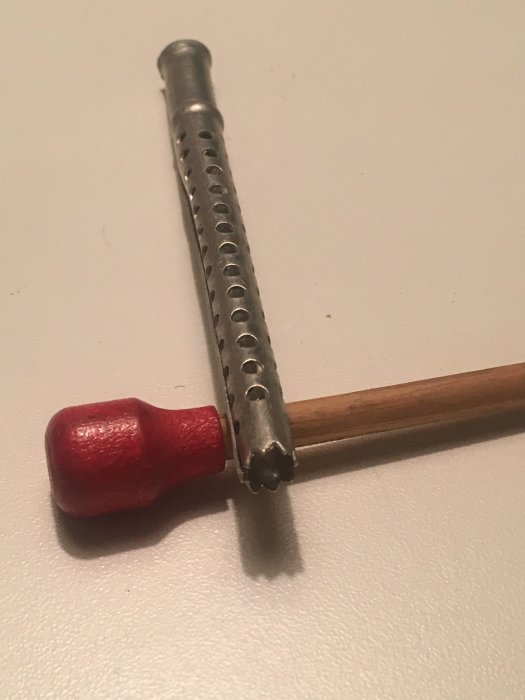 Äldre köksredskap i aluminium med en taggad ände och ett rött handtag, möjligen för kryddning.