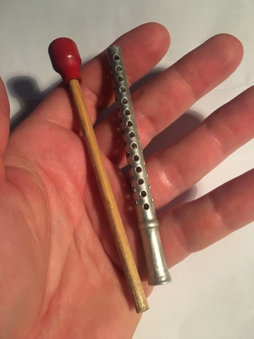 En person håller en liten, klen aluminiumstång jämfört med en tändsticka i handen.