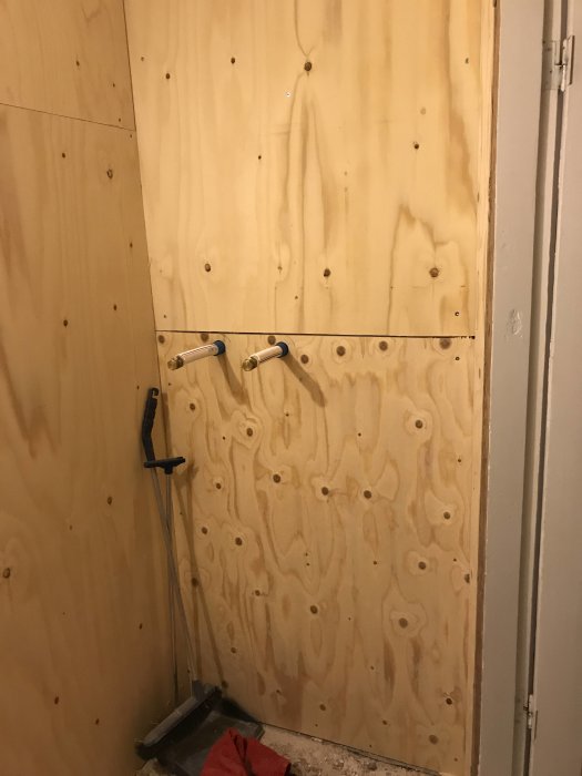 Installation av 15mm tjock plywood på en vägg med synliga röranslutningar.