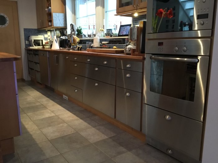 Kök med uppdaterade rostfria luckor och lådfronter, diskmaskin och ugn i ett heminredningsprojekt.