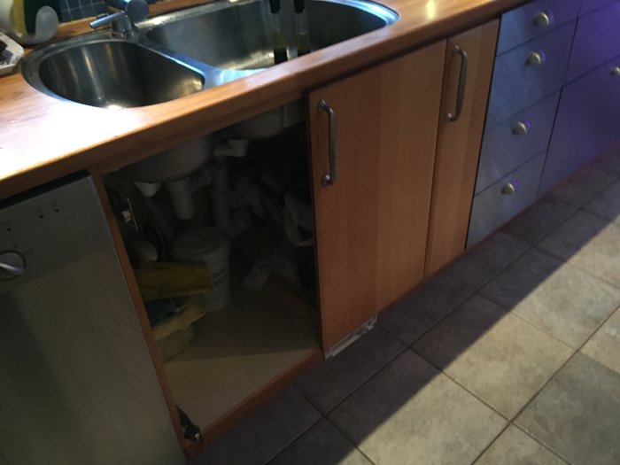 Köksskåp under uppgradering med öppen skåpdörr, saknar front, och intilliggande blåa lådfronter.