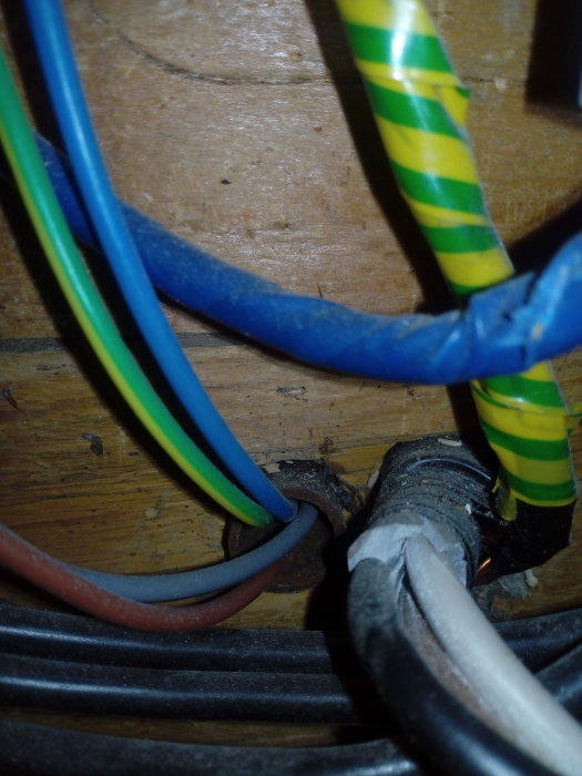 Elektriska kablar i olika färger går genom en trävägg via genomföringshål.
