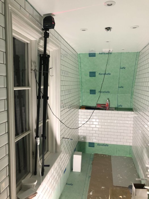 Renoveringsarbete i badrum med kaklade väggar och gröna byggplattor, laserinstrument för mätning aktiverat.