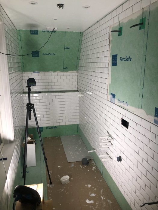 Renoveringsprojekt av badrum med kaklade väggar, vattentätning och en tripod på golvet.