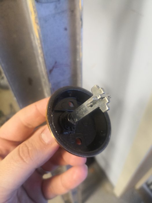 Hand som håller en demonterad låscylinder till en Assa 2000 garagedörr med synligt korsslag.