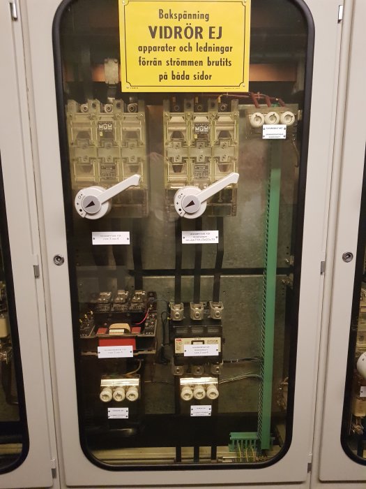 Inredning av elektriskt skåp med kontaktorer och varningsskylt "Bakspänning - VIDRÖR EJ".