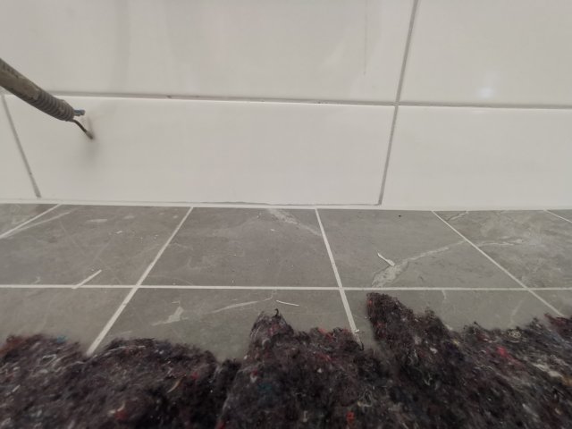 Ojämnt kakelarbete vid golv och silikonlagning, med synliga glipor och dålig finish.