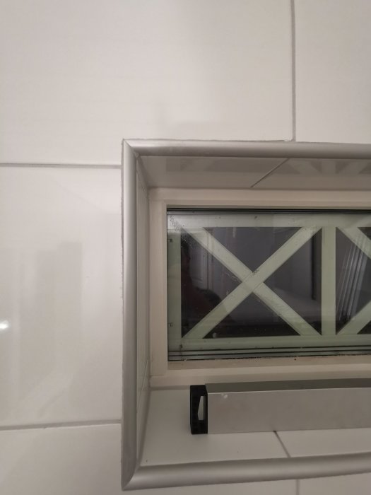 Närbild på kakelarbete runt ett fönster i badrum med synligt ojämnt och flisigt finish.