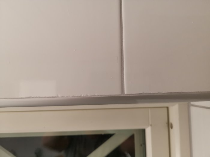 Närbild på ojämn och flisig fogning mellan kakel och fönsterkarm i badrum.