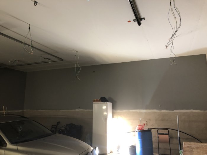 Garage under renovering med lösa sladdar från taket, en bil och byggmaterial synliga.