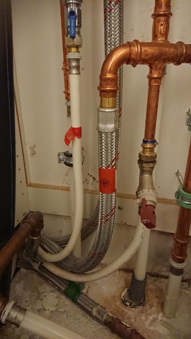 Komplex rörinstallation med blandning av koppar och plastledningar, inkluderar ventiler och isolering.