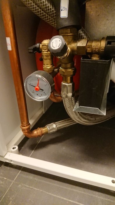 Koppar och metallrör med mätare, ventil och stålflätad slang för fjärrvärmeinstallation.