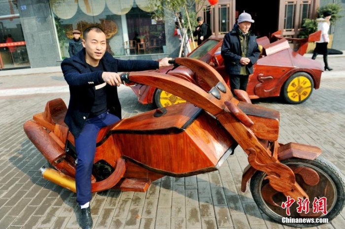 Man som sitter på en handgjord motorcykel skulpterad i trä på en stadsgata.
