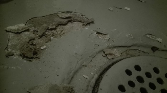Flagnat betonggolv med avflagningar nära en avloppsbrunn.