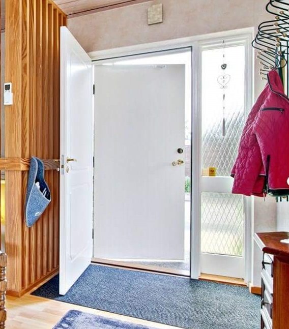 En öppen vit innerdörr med tjockare lister, intill ett fönster med rutmönstrat glas och klädhängare.