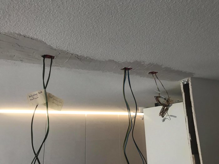 Öppen vägg med synliga elektriska kablar och noteringar som hänger från taket.