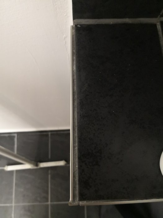 Närbild på dålig plattsättning i ett hörn av ett badrum med svarta kakelplattor och ojämn fog.