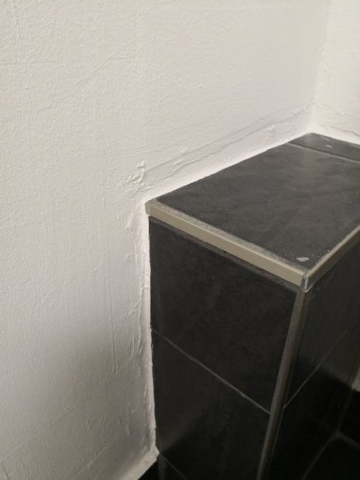 Ojämn plattsättning och putsning i ett hörn mellan vägg och kaklad kant.
