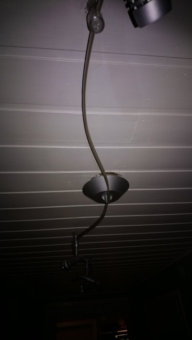 Bild på en slingrig belysningsarmatur monterad i ett vitt trätak, med kablar och spotlights.