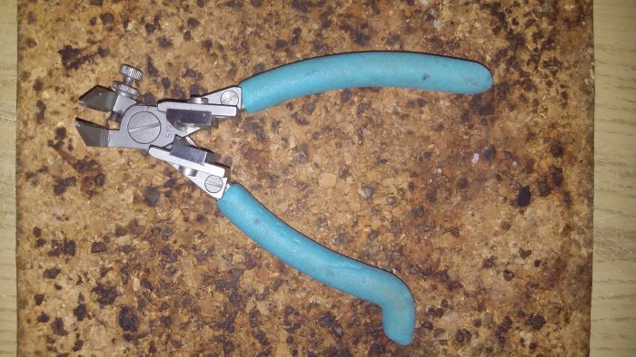 Använd kabelskalarklippare med blå handtag och slitage på käftarna, liggande på korkunderlag.